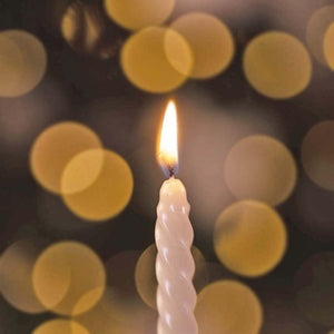 White candle with a flame against a blurred background of lights
