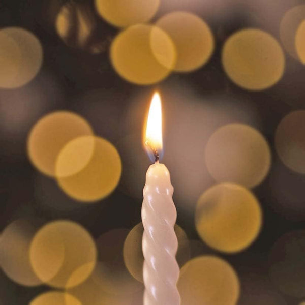 White candle with a flame against a blurred background of lights