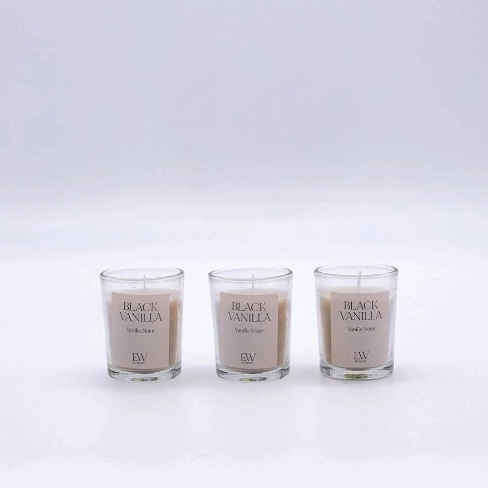 Three 'Black Vanilla' candles on a wooden surface with a plant in the background