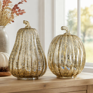 Two ribbed glass effect pumpkins with gold glitter, displayed on a wooden table in a decorated indoor setting.
