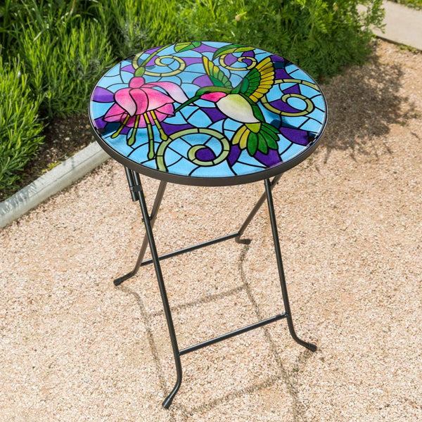 Colorful stained-glass table with floral designs on a gravel surface.