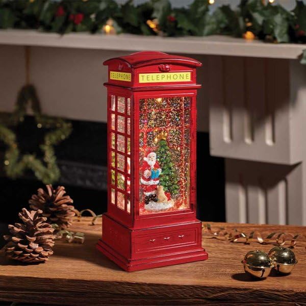 Decorative red telephone booth with a Christmas scene inside, on a wooden surface.