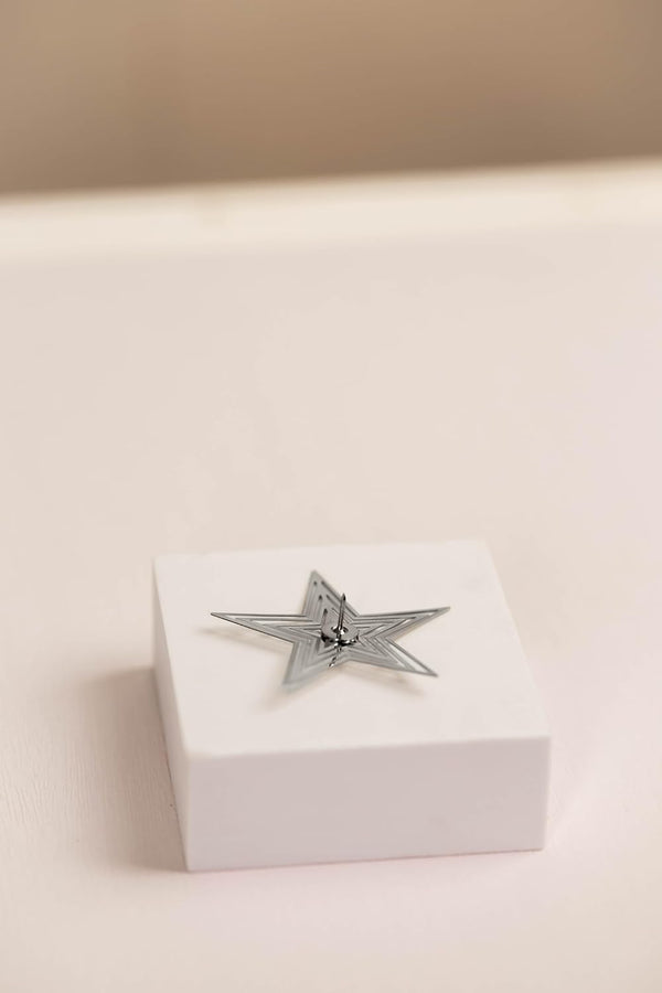 Silver star-shaped object on a white box with a beige background