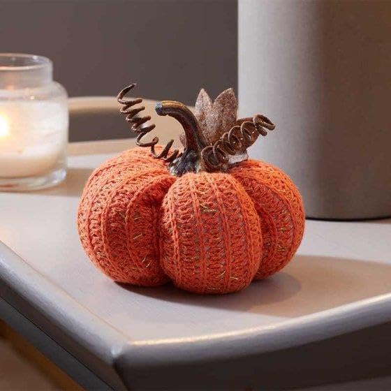 Knitted pumpkin decoration with decorative leaves on a surface.