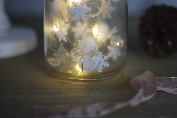 Glass jar with snowflake decorations and LED lights on a wooden surface
