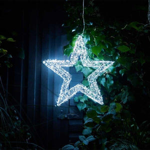 Decorative LED star hanging among green leaves at night