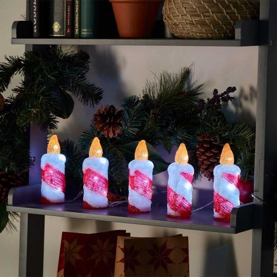 Decorative candles with candy cane design on a shelf with Christmas decorations.