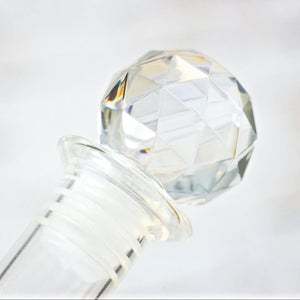 Clear glass bottle with a faceted stopper on a white background