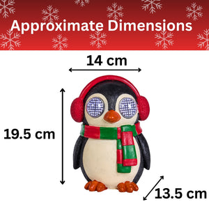 A penguin figurine wearing red earmuffs and a red-and-green striped scarf, shown with measurement arrows and labels indicating approximate dimensions: 14 cm wide, 19.5 cm tall, and 13.