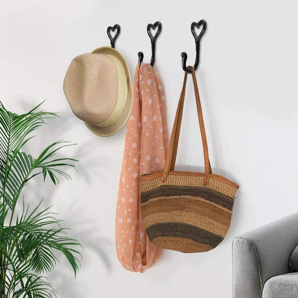 Three heart-shaped hooks on a white wall with a hat, towel, and bag hanging from them.