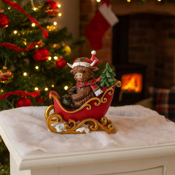 Decorative figurine of a child in a sleigh with a Christmas tree, in front of a fireplace and Christmas tree.