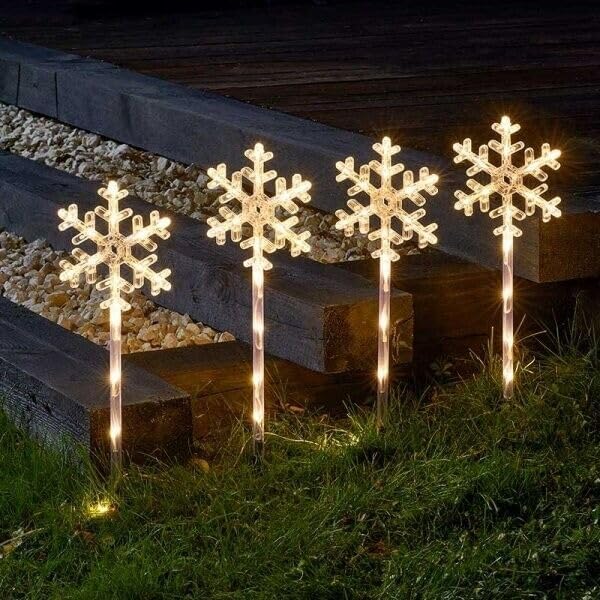 Four snowflake-shaped outdoor lights on a wooden platform with grass and stones in the background.