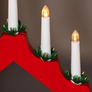 Decorative candles with greenery on a red stand against a brown background