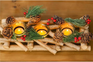 Decorative arrangement with candles, pine cones, and greenery on a wooden surface.