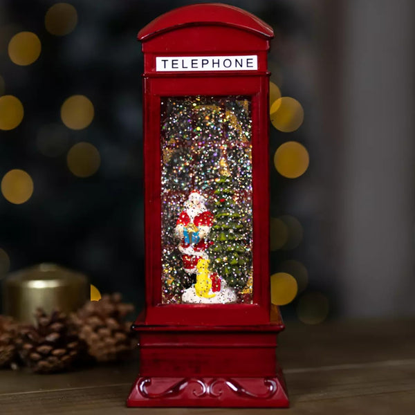 Red telephone booth snow globe with Santa Claus figure and Christmas tree against a blurred background
