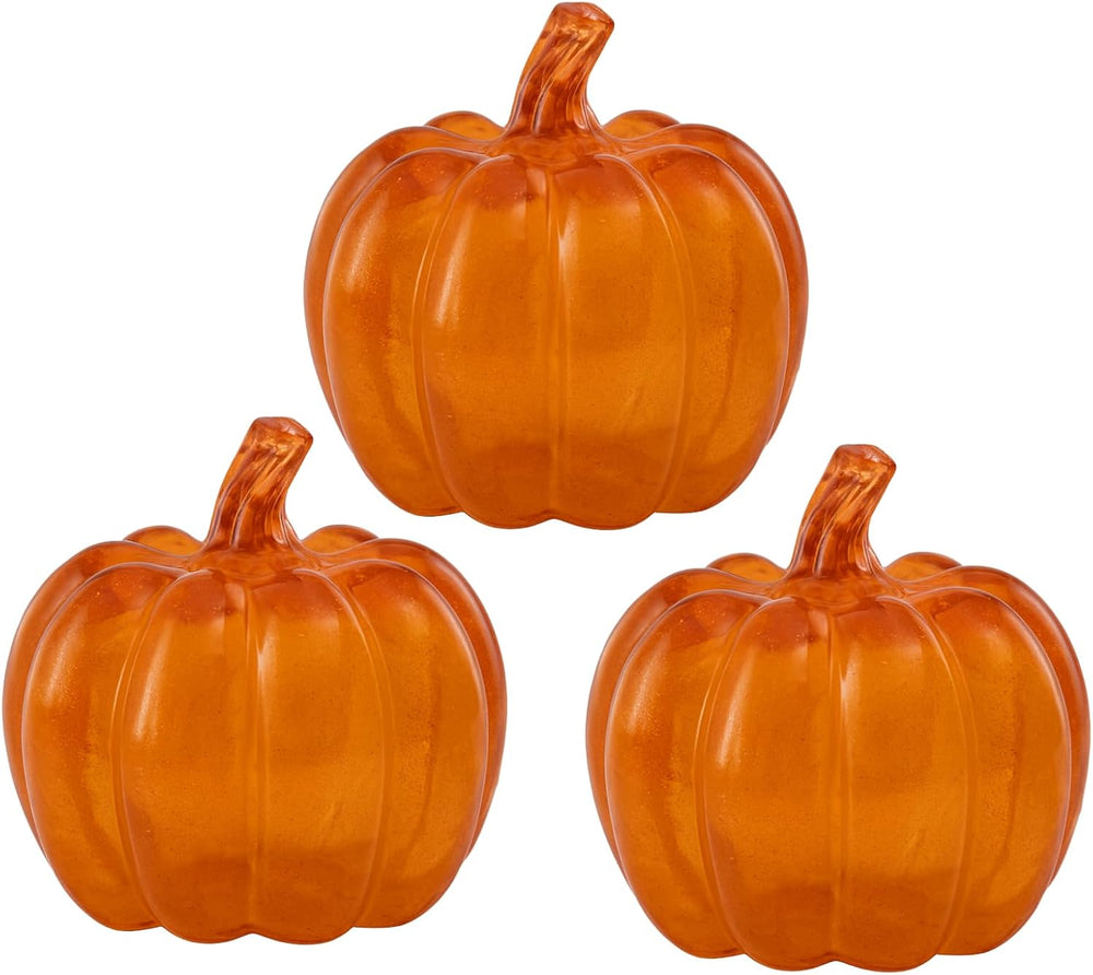 Three glowing orange glass pumpkins on stacked books with a warm glow.