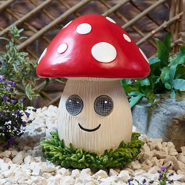 Mushroom-shaped garden light with a smiling face on a pebble surface with plants in the background