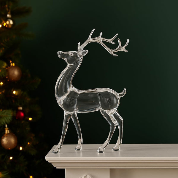 Clear glass deer ornament on a mantelpiece with a Christmas tree in the background