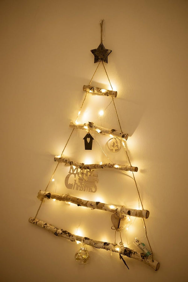 Decorative wall-mounted Christmas tree made of branches with lights and small ornaments on a plain wall.