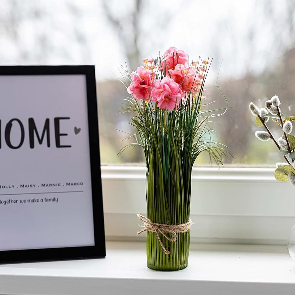 Vase with pink flowers on a windowsill next to a framed picture with 'HOME' text.