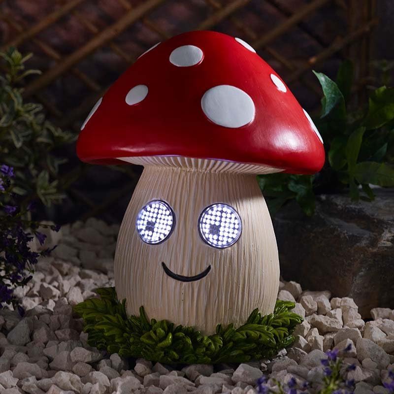 Mushroom-shaped night light with a red cap and white spots, sitting on a stone surface with plants in the background.