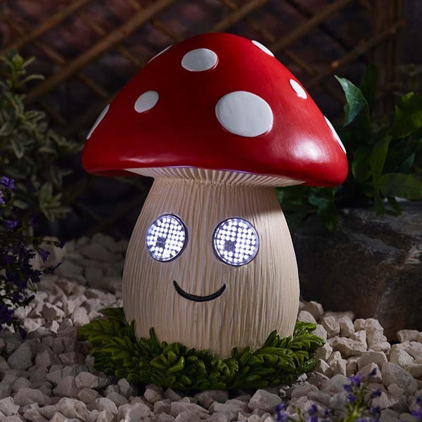 Mushroom-shaped night light with a red cap and white spots, sitting on a stone surface with plants in the background.