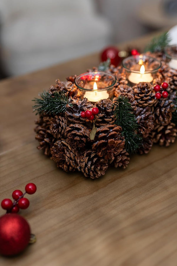 Decorative arrangement of pine cones with candles and red berries on a wooden surface.