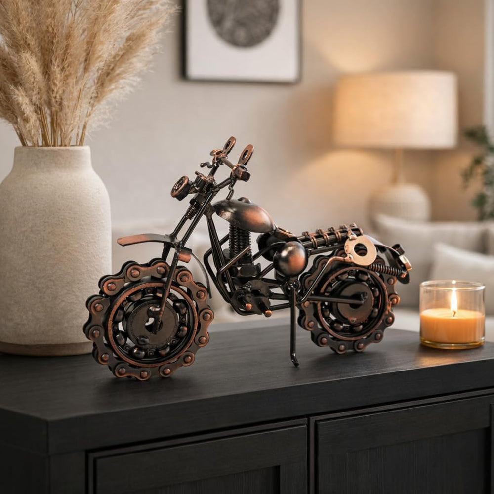 Decorative metal motorcycle sculpture on a table with a candle and vase in the background.