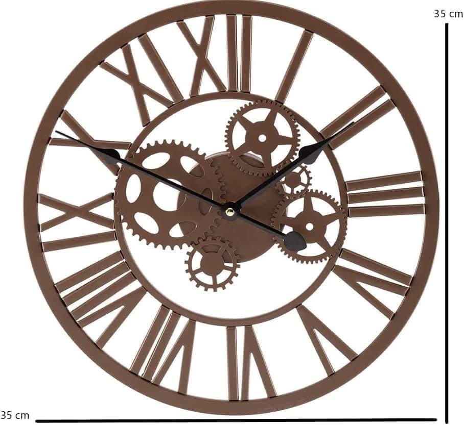 A vintage bronze wall clock with Roman numerals and a skeleton gear design, mounted on a wall with a plant branch in the background.