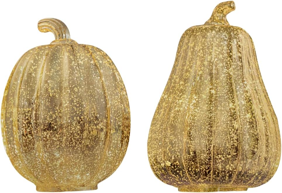 Two glittery pumpkin-shaped lamps on a reflective surface with candles and a basket in the background.