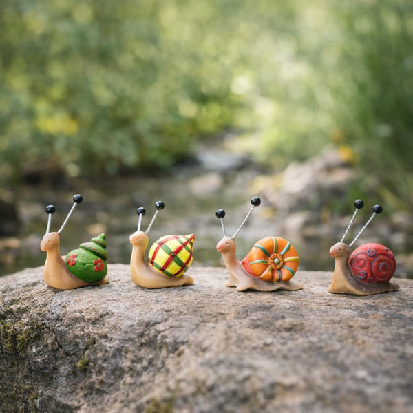 Four decorative snail figurines with colorful shells on a rock with a natural background.