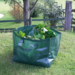 A green plastic garden waste bag filled with green leaves and branches, sitting on a grassy lawn outdoors near a fence and tree.