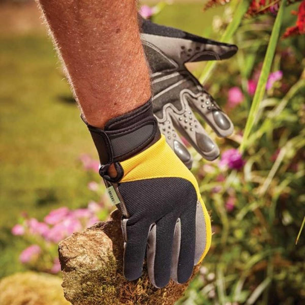 A person wearing a pair of black, gray, and yellow gardening gloves with rubberized grips is holding a plant.