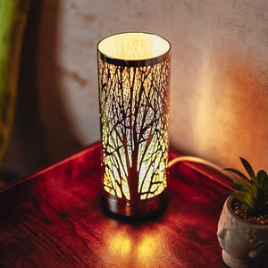 Decorative table lamp with tree branch design on a wooden surface.