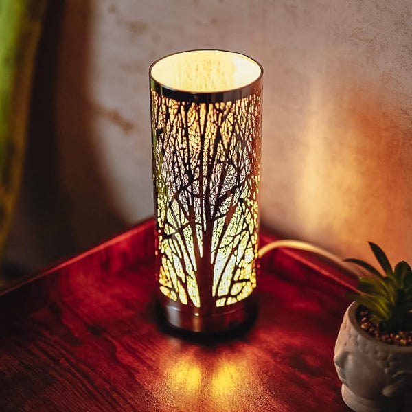 Decorative table lamp with tree branch design on a wooden surface.