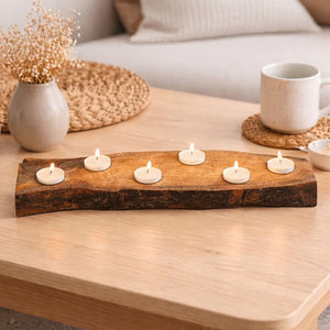 A rustic wooden tea light candle holder with five lit tealight candles, styled on a light wood coffee table in a cozy living room setting.