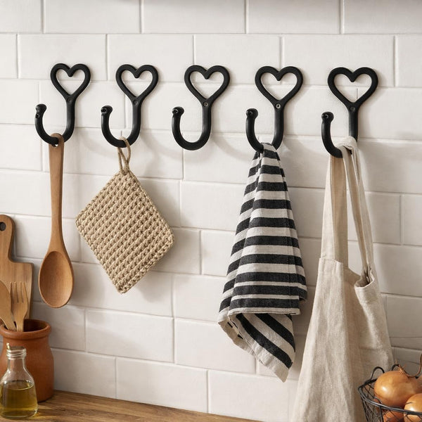 Heart-shaped hooks on a tiled wall with kitchen items hanging from them.