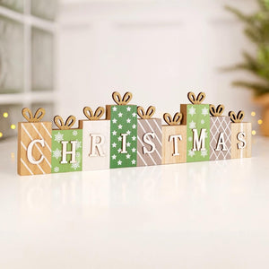 Wooden Christmas letter sign spelling CHRISTMAS, styled as wrapped gift boxes in green, beige, white, and brown patterns, with small wooden bows on top, displayed on a white surface.