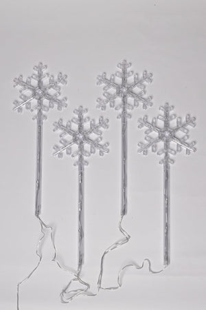 Set of four silver snowflake-shaped cake toppers on sticks against a light gray background.