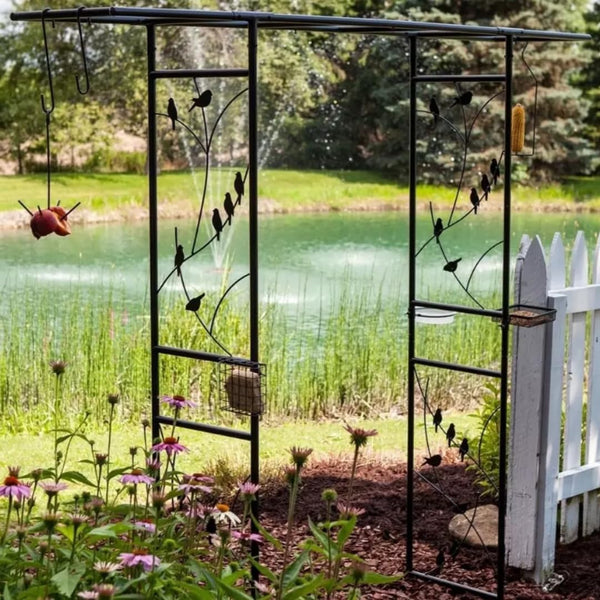 Decorative metal garden arch with bird designs in a garden setting with a pond in the background.