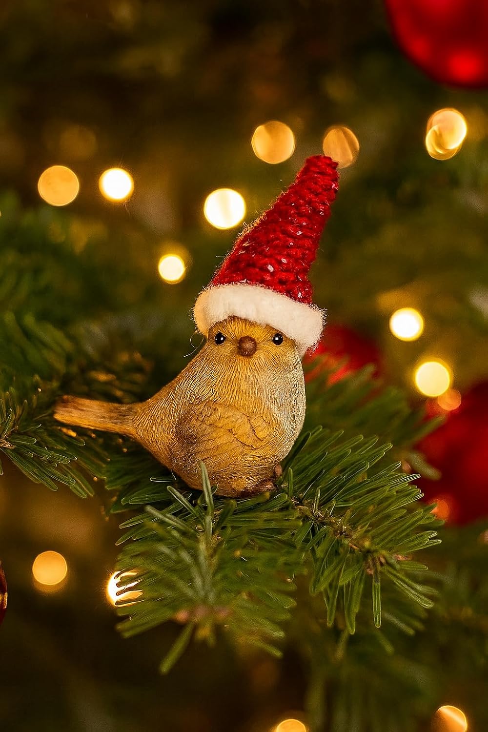 Small bird figurine wearing a Santa hat on a Christmas tree with blurred lights in the background