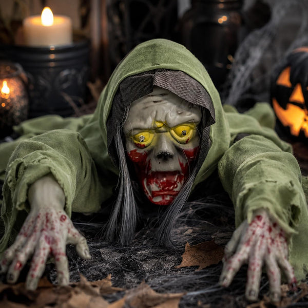 A creepy Halloween decoration of a hooded zombie or skeleton figure crawling forward, wearing a tattered green hood and stained with red blood, with glowing yellow eyes and gray hair, set against a dark spooky background with candles and a jack-o'-lantern.