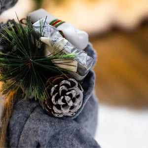 Person wearing a gray coat with a pine cone and greenery accessory, blurred background
