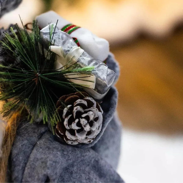 Person wearing a gray coat with a pine cone and greenery accessory, blurred background