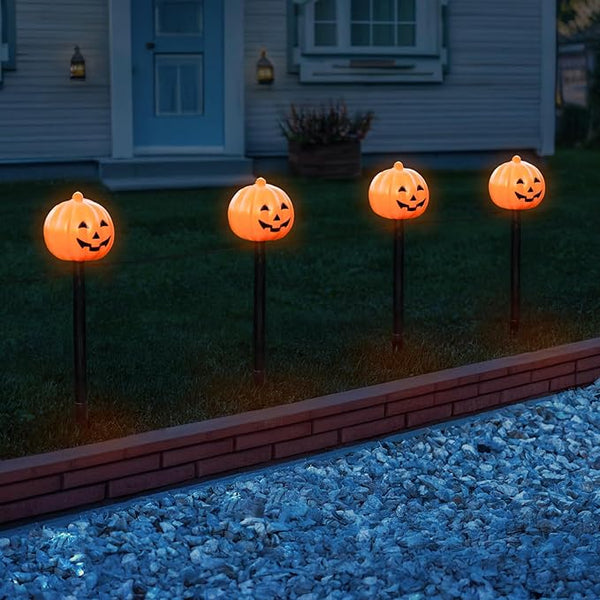 Four pumpkin-shaped lights on stakes in front of a house
