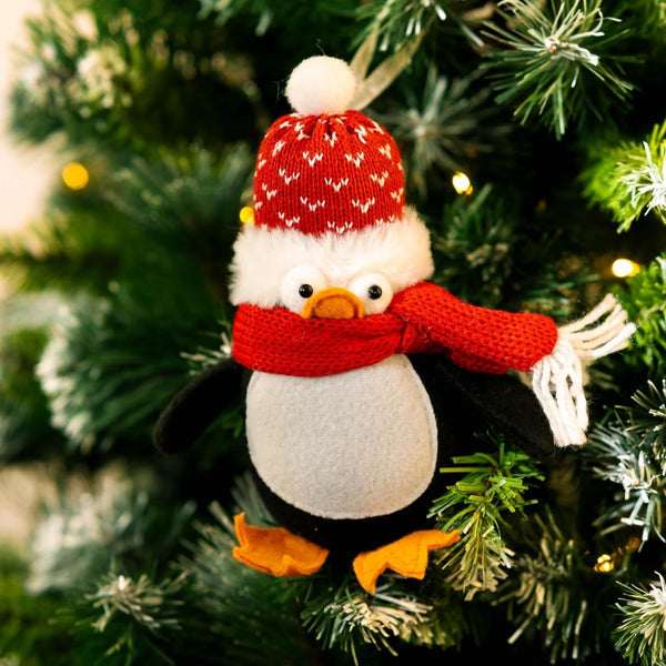 Knitted penguin ornament with a red hat and scarf on a Christmas tree.