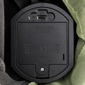 Close-up of a black plastic battery compartment cover with a switch labeled OFF/ON and TRY ME, showing embossed text 'MADE IN CHINA' and product symbols, set against dark fabric and olive green mesh.