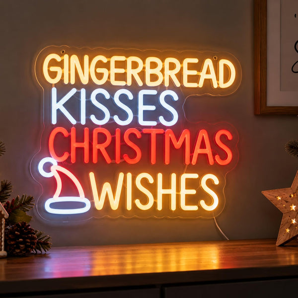 A glowing LED neon-style sign on a wall above a wooden surface, reading “GINGERBREAD KISSES CHRISTMAS WISHES” in warm yellow, white, and red lettering, with a small white Santa hat graphic. Decorative pinecones and a star-shaped light sit nearby.