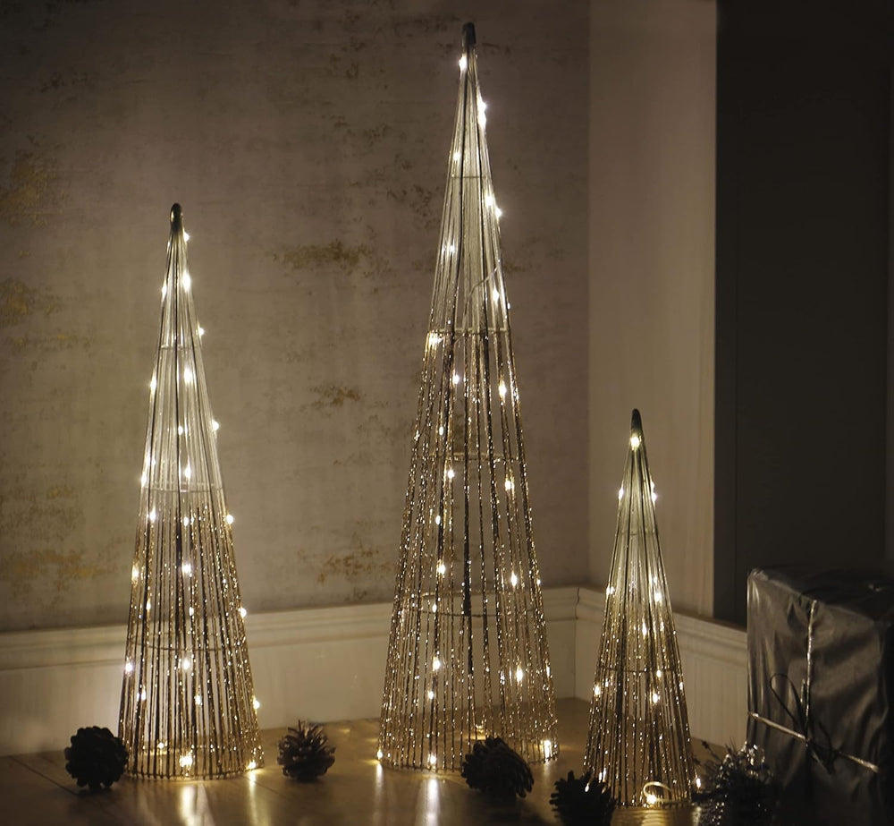 Three decorative LED trees on a wooden floor against a textured wall.