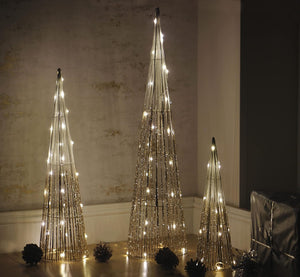 Three decorative LED trees on a wooden floor against a textured wall.